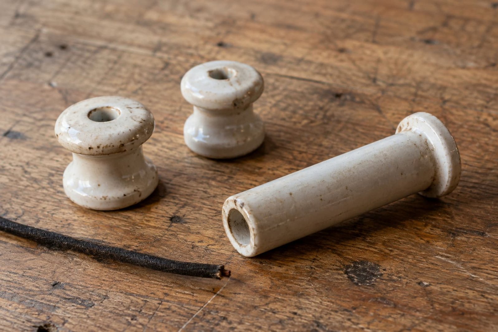 Two loose porcelain support knobs, a hollow insulating tube and a disconnected cloth-covered wire sample on a workbench.